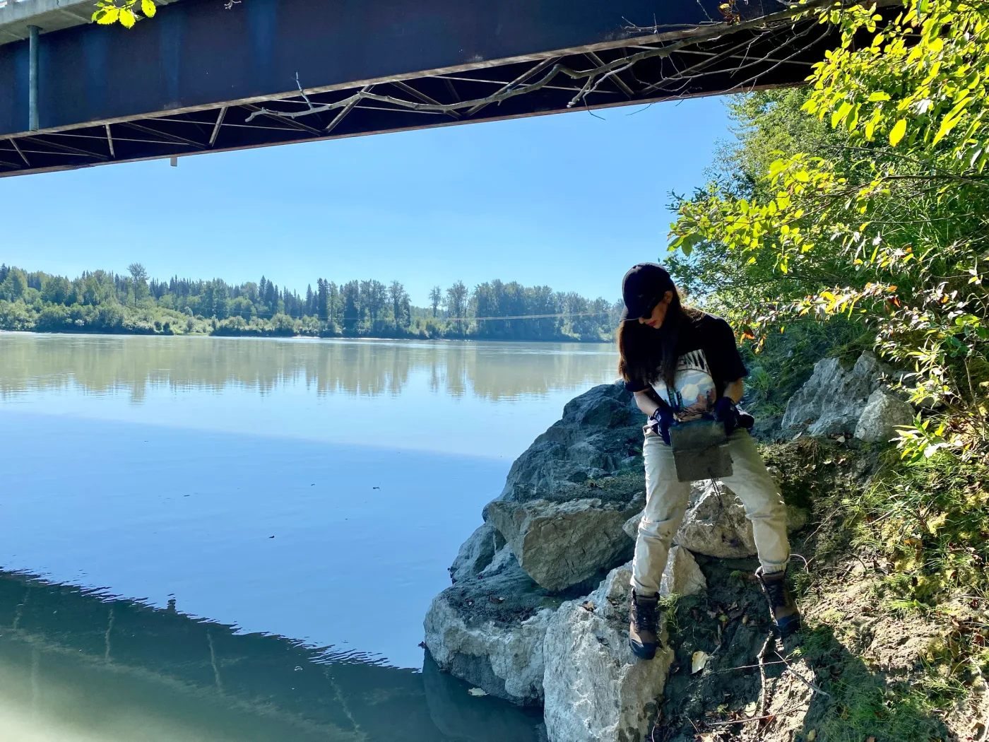 Behnoosh working with equipment on a rocky riverbank beneath a bridge