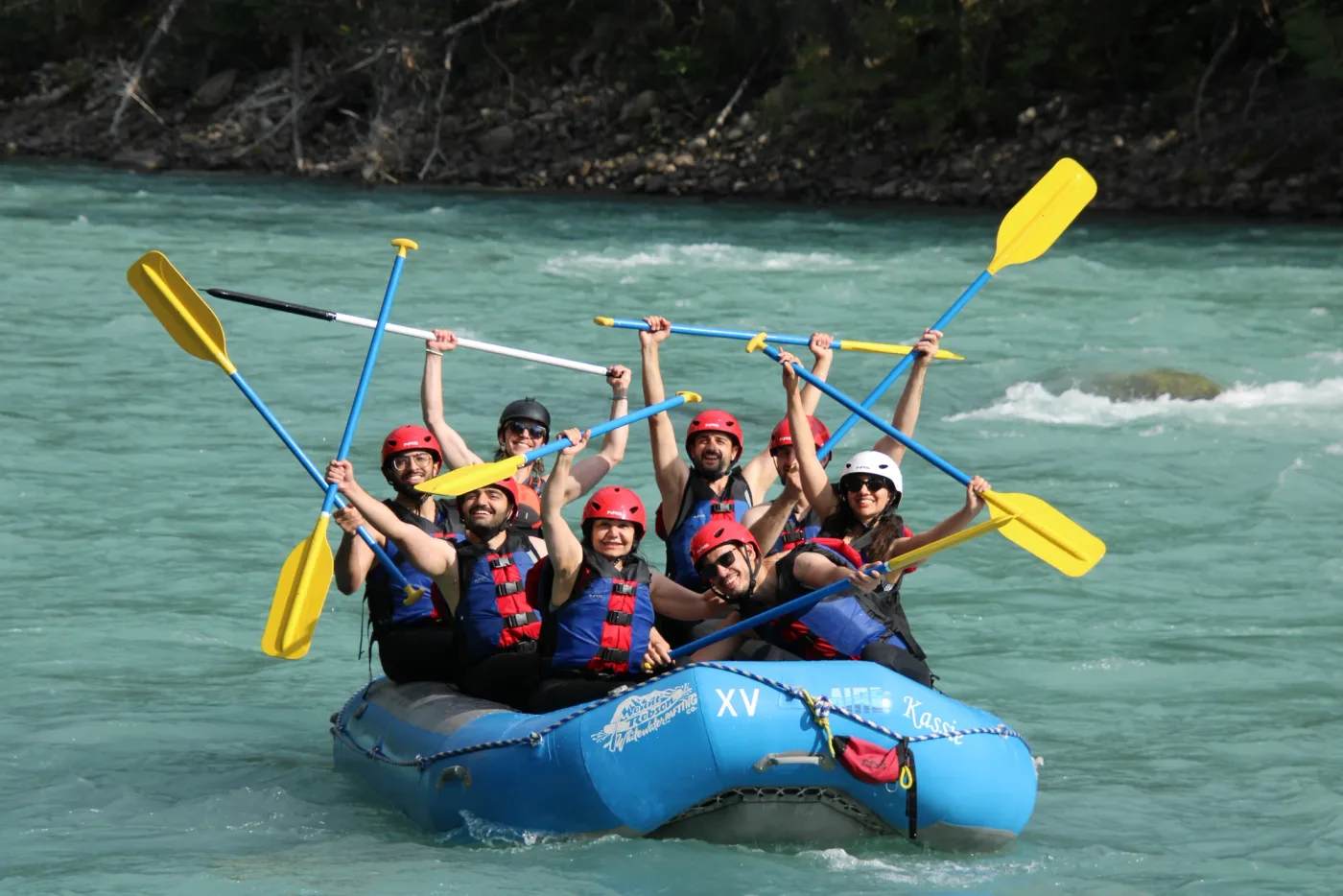 A group in a blue raft holding paddles above the water.